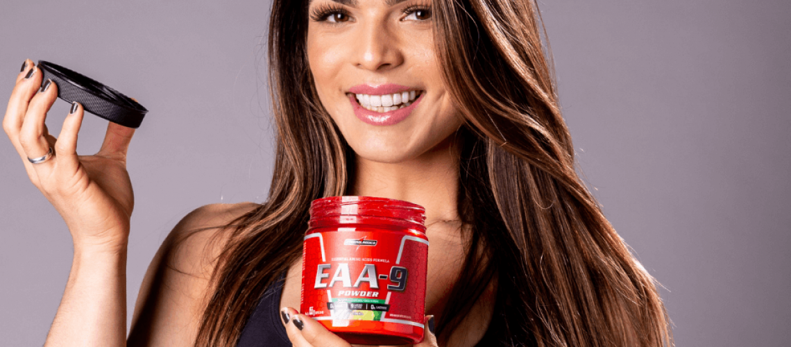mulher sorrindo e segurando pote vermelho de aminoacidos essenciais